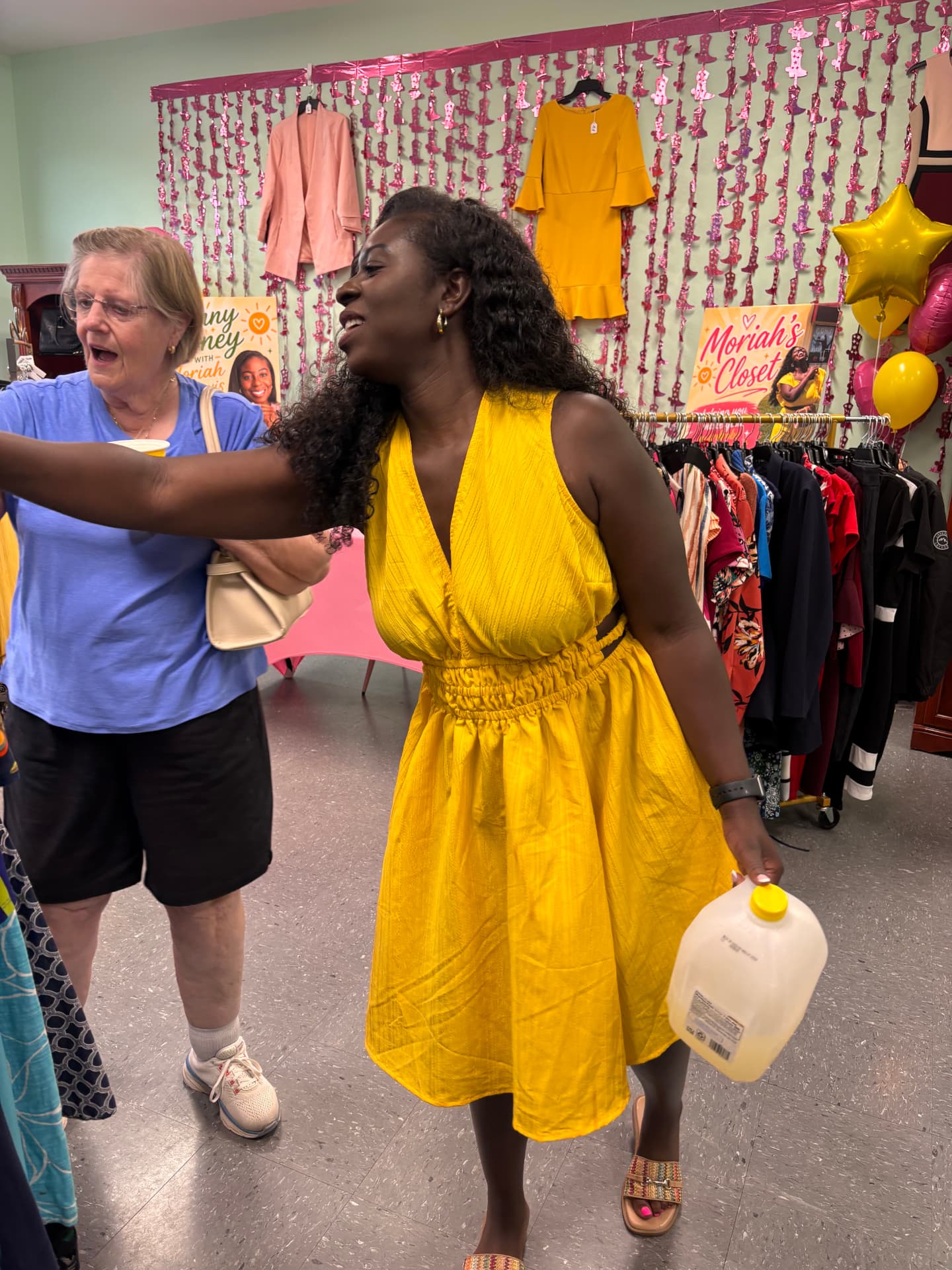 Moriah Davis laughing in a yellow dress while helping a shopper at Moriah's Closet