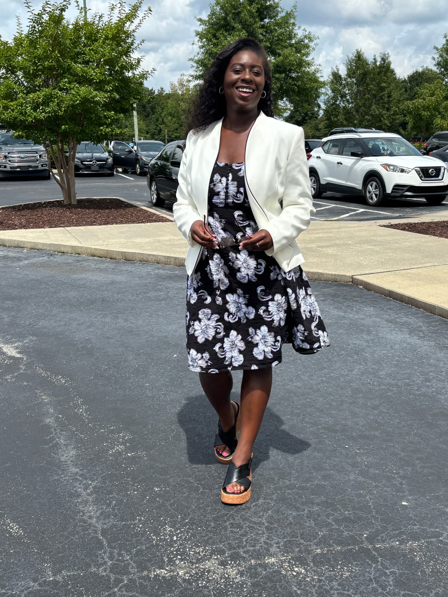Moriah Davis smiling in a white blazer and black floral dress outdoors