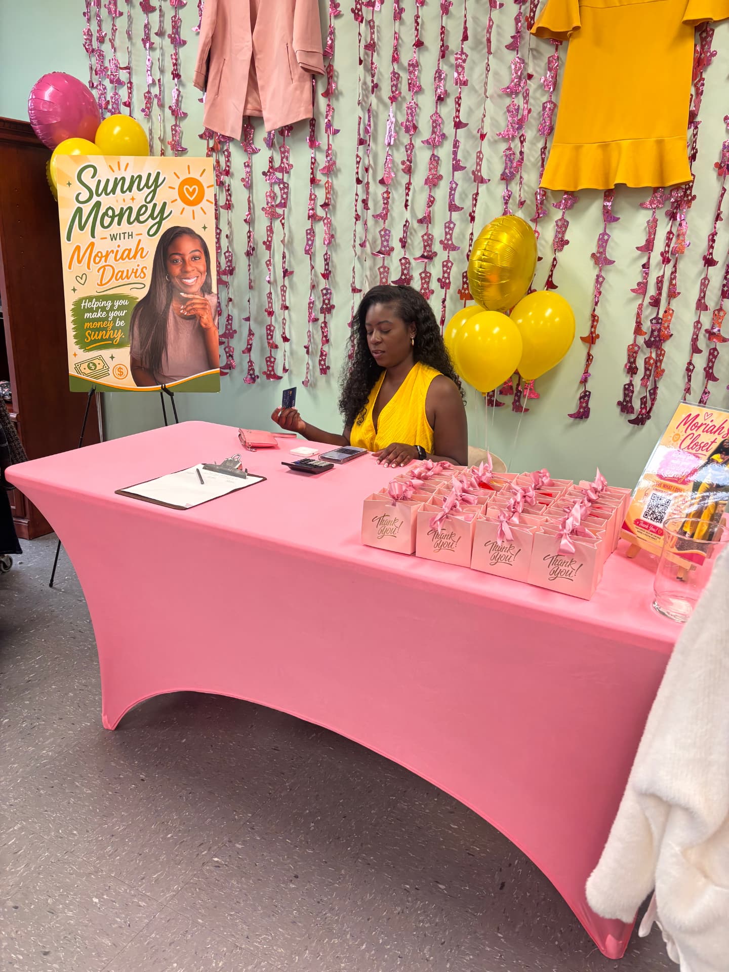 Moriah Davis at the Sunny Money check-out table at Moriah's Closet, surrounded by pink thank-you gift boxes and balloons